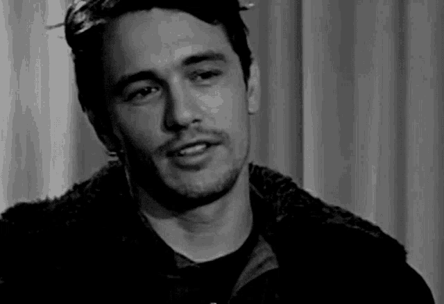 a black and white photo of a man wearing a fur jacket and a black shirt .