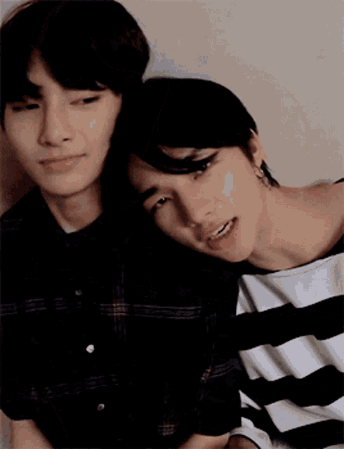 two young men are sitting next to each other and one is wearing a striped shirt