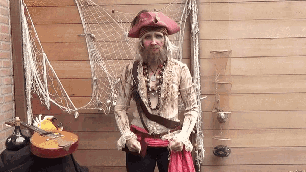 a man dressed in a pirate costume stands in front of a wooden wall