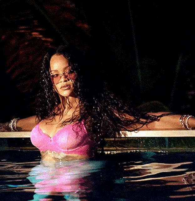 a woman in a pink bra is standing in a pool at night