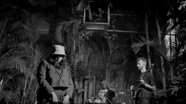 a black and white photo of a group of people playing instruments in a room with palm trees .