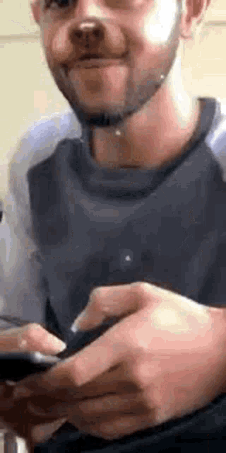 a man with a beard is holding a cell phone and wearing a dog nose .