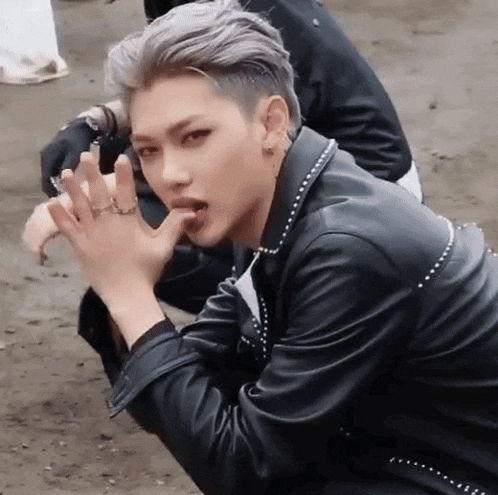 a young man with gray hair is wearing a black leather jacket and is kneeling down .