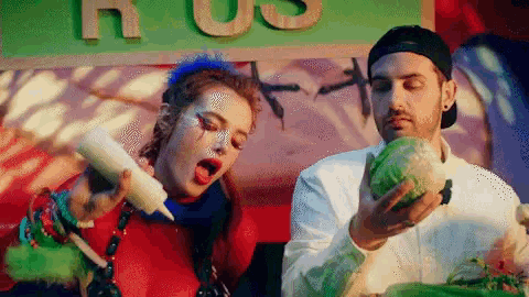 a woman is pouring sauce on a man 's head while he eats a cabbage