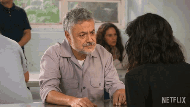 a man sits at a table with a woman behind him and a netflix logo behind him