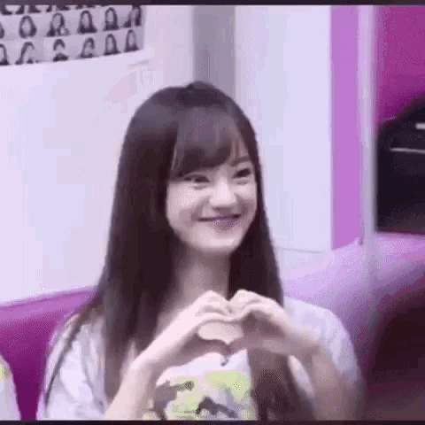 a woman is making a heart shape with her hands while smiling .