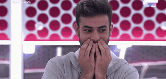 a man with a beard is covering his mouth with his hands in front of a polka dot wall .