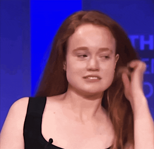 a woman with long red hair is standing in front of a blue wall with the letter t on it