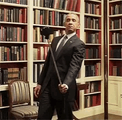 a man in a suit and tie is standing in front of a bookshelf holding a stick