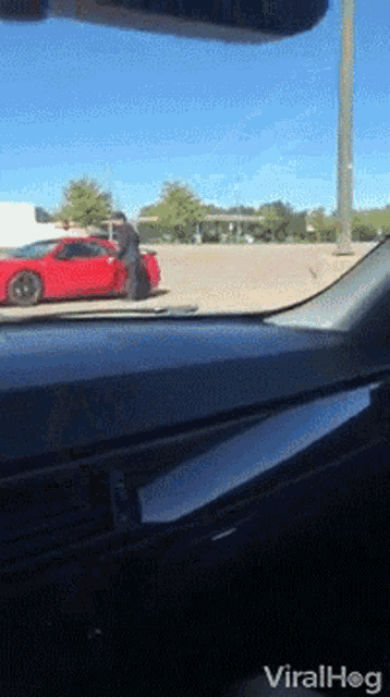 a red car is parked in a parking lot next to a man