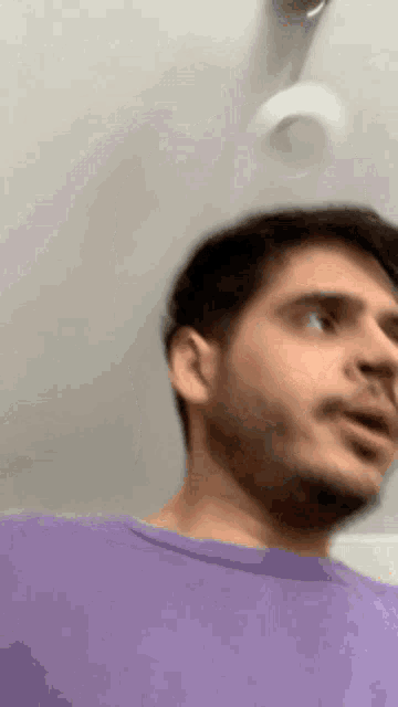 a man with a beard is wearing a purple shirt and looking at something .