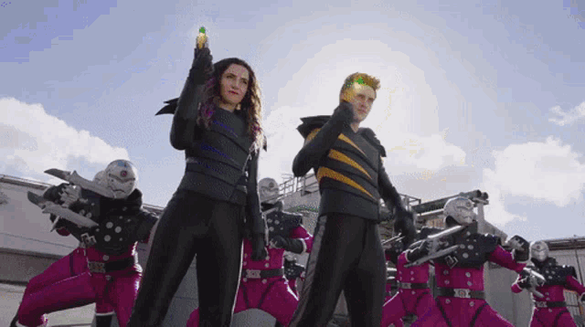 a man and a woman are standing in front of a group of people in pink jumpsuits