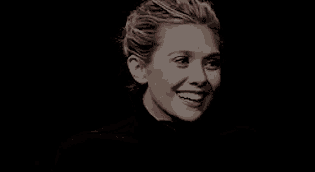 a close up of a woman 's face with a black background smiling