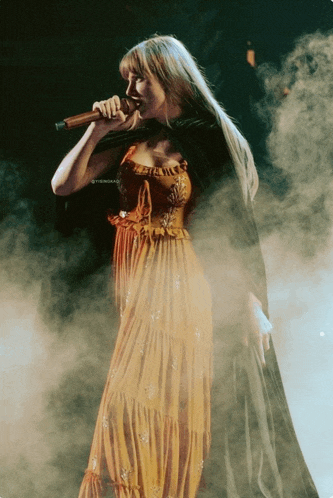 a woman in a long orange dress singing into a microphone on stage