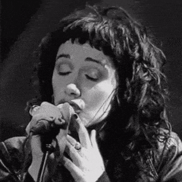a woman is singing into a microphone while wearing a leather jacket .