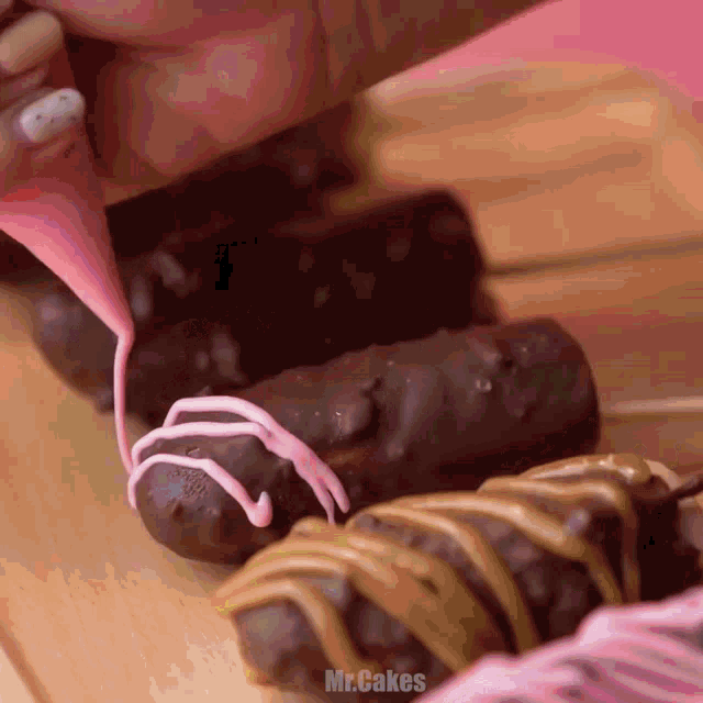a person is decorating a chocolate bar with pink frosting and the words mr.cakes below it