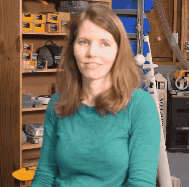 a woman in a blue shirt is sitting in front of a shelf with boxes on it