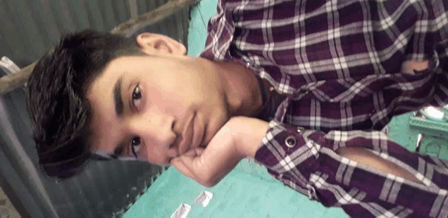 a young man in a purple plaid shirt rests his head on his hand