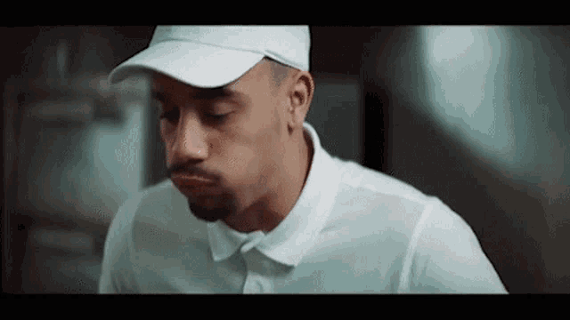 a man wearing a white hat and a white polo shirt is looking down .