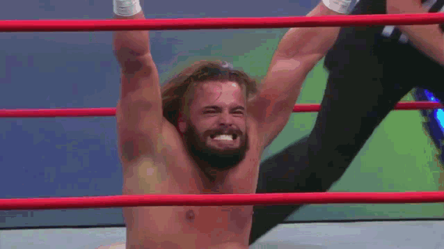 a shirtless wrestler is hanging upside down in a ring