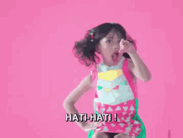 a little girl is sitting on a chair with her hands on her hips and says hati-hati !