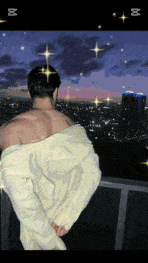 a shirtless man stands on a balcony looking out over a city at night