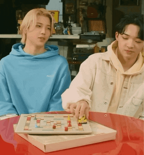 a man in a blue hoodie is playing a board game with another man in a white jacket