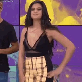 a woman in a black top and plaid pants stands with her hands on her hips
