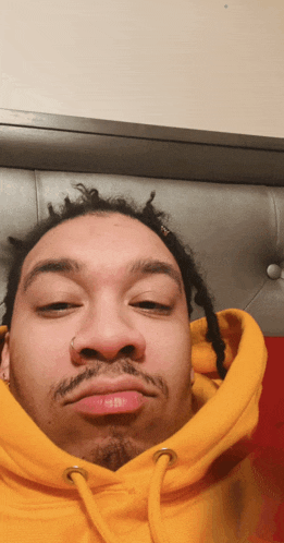a man with dreadlocks is wearing a yellow hoodie and making a funny face