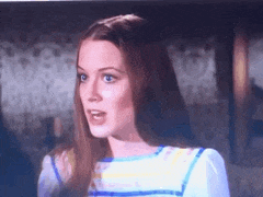 a woman with long red hair and blue eyes is wearing a blue and white striped shirt .