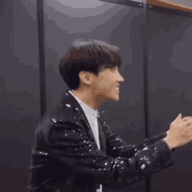 a man in a black sequined jacket is clapping his hands in a room .