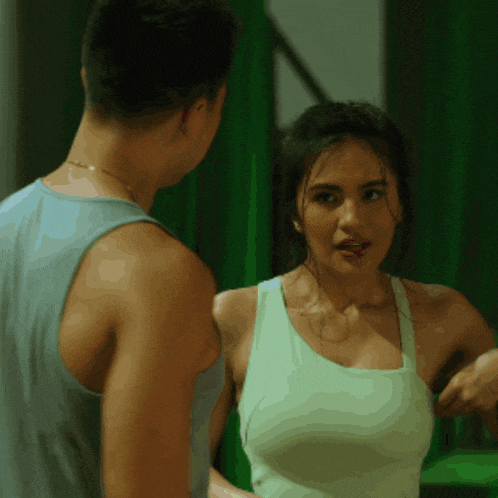 a man and a woman are standing next to each other and the woman is wearing a white tank top