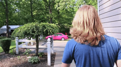 a man in a blue shirt walks down a sidewalk towards a pink car
