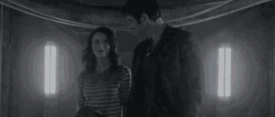 a man and a woman are standing next to each other in a dark room holding hands .