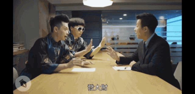 a man in a suit sits at a table talking to two young men