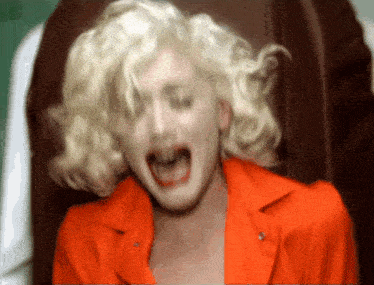 a woman with blonde hair is wearing an orange jacket and screaming