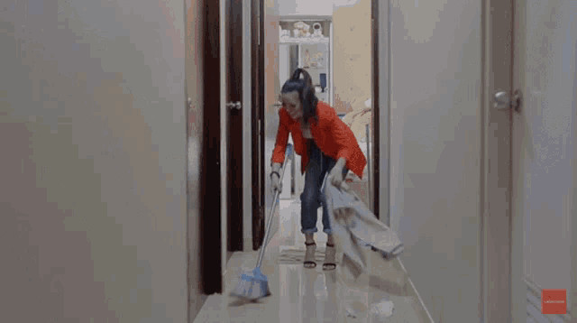 a woman in an orange jacket is mopping a hallway