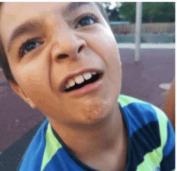 a young boy is smiling and looking up at the camera while wearing a blue and green shirt .
