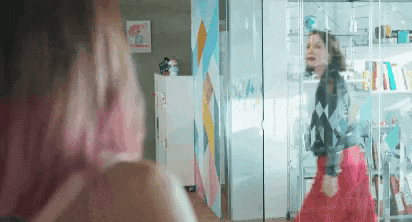 a woman with pink hair is standing in front of a glass wall .