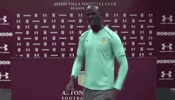 a man is standing in front of a wall that says ' aston villa football club ' on it .
