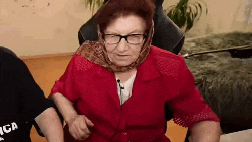 an elderly woman wearing glasses and a scarf around her head is sitting in a chair in a living room .