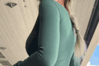 a woman wearing a green sweater and a braided ponytail is standing on a balcony .