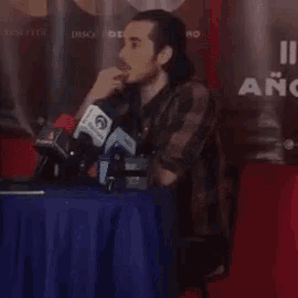 a man sits at a table with microphones in front of a sign that says " año " on it