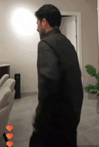 a man in a black jacket is standing in a room with the name jaco on the bottom right corner