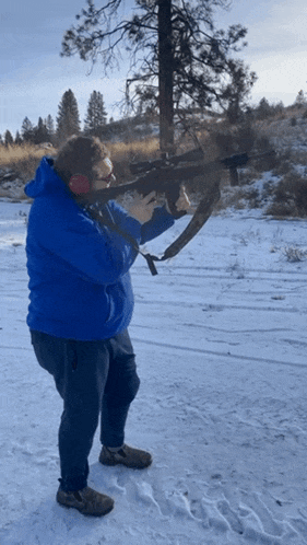 a man in a blue hoodie holds a gun in the snow