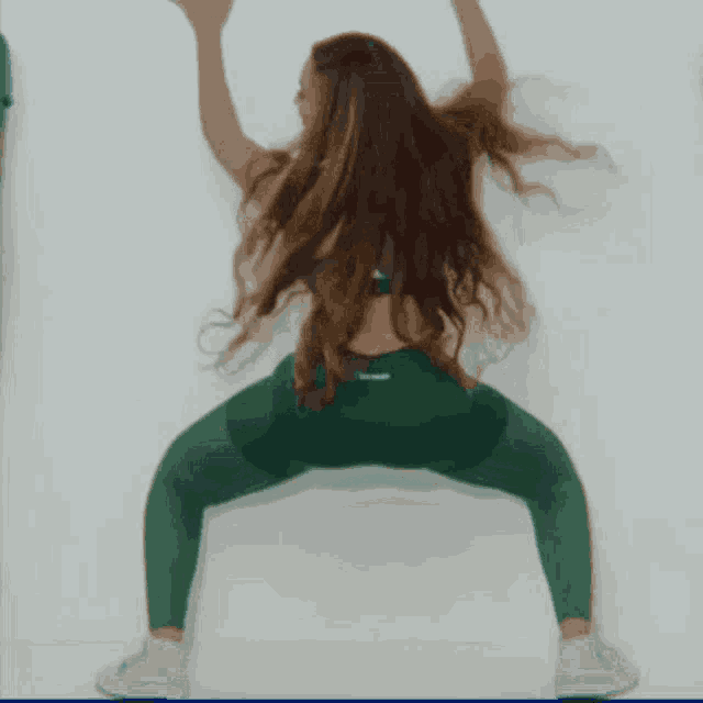 a woman with long hair is doing a squat with her arms up