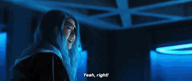 a woman with blue hair is standing in a dark room with blue lights and says `` yeah , right ! ''