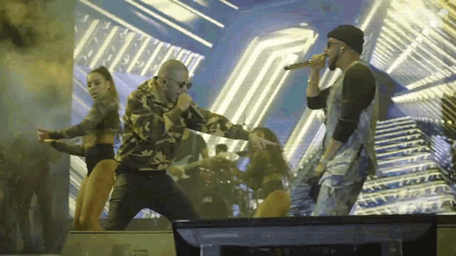 a man is singing into a microphone while two women are dancing in front of him