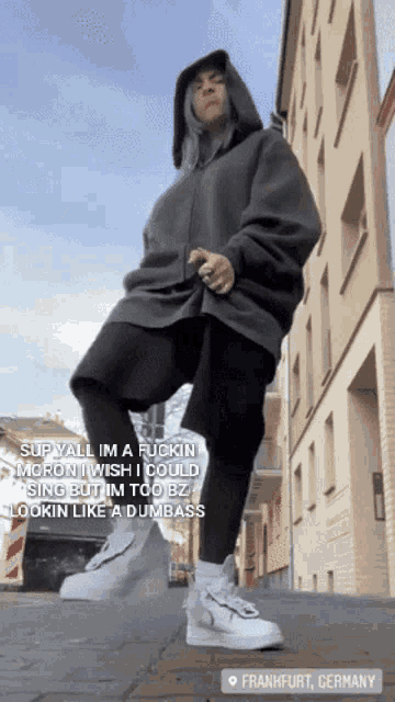 a person in a grey hoodie is standing on a sidewalk in front of a building