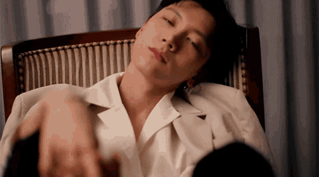 a young man in a white shirt is laying in a chair with his eyes closed